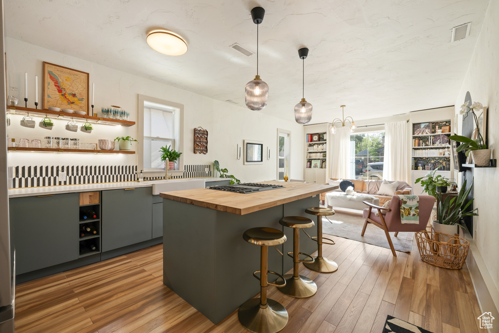 Kitchen featuring butcher block counters, stainless steel gas stovetop, a breakfast bar area, light wood-style flooring, and open shelves