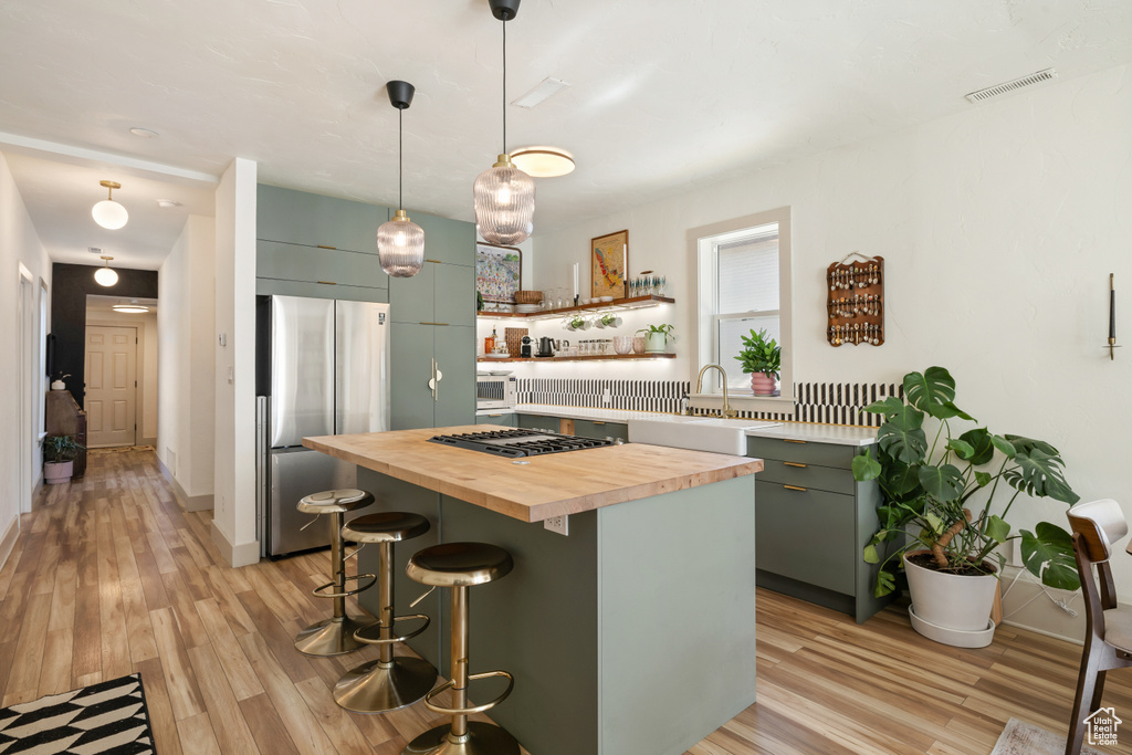 Kitchen with butcher block counters, appliances with stainless steel finishes, open shelves, a breakfast bar, and light wood-style floors