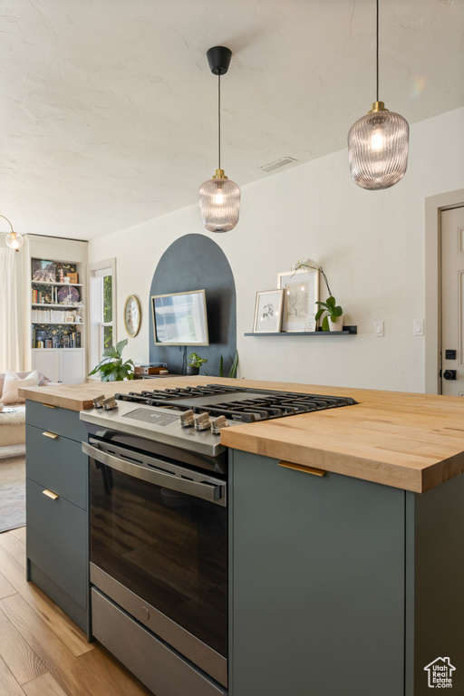Kitchen with wood counters, gas stove, gray cabinets, light wood-type flooring, and hanging light fixtures