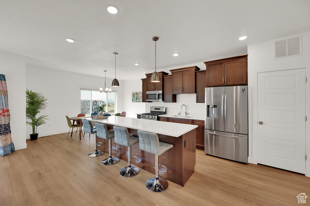 Kitchen featuring appliances with stainless steel finishes, a breakfast bar, a kitchen island, light wood-style flooring, and recessed lighting