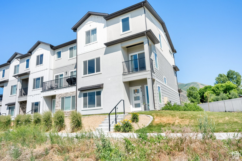 Back of house featuring stone siding, stucco siding, and a balcony