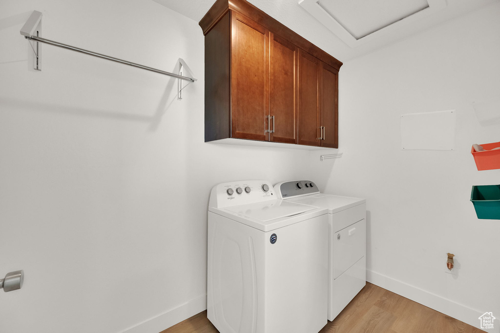 Washroom with cabinet space, separate washer and dryer, attic access, and light wood-style flooring
