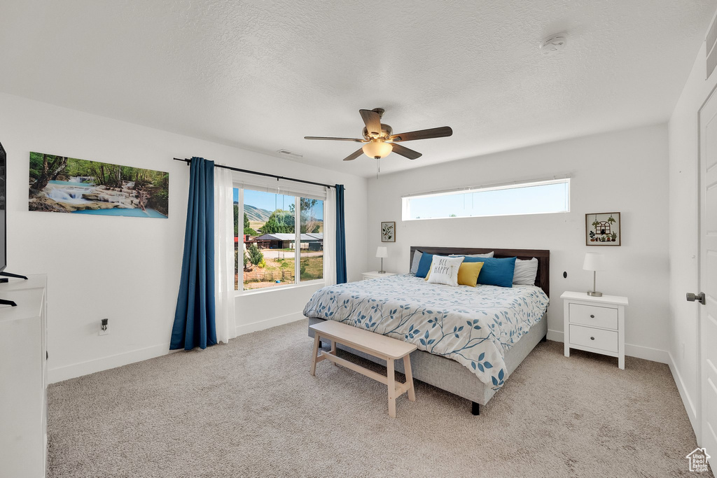 Bedroom with light colored carpet, a textured ceiling, and ceiling fan