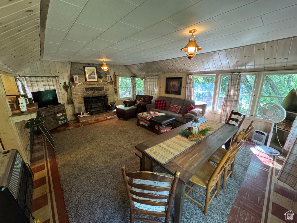 Carpeted dining room with wooden walls, a fireplace, and vaulted ceiling