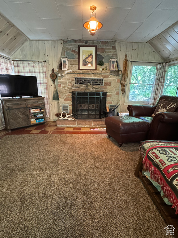 Living area with lofted ceiling, wood walls, a stone fireplace, and carpet floors