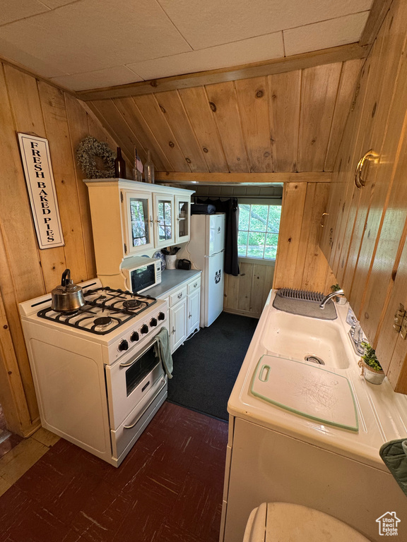 Kitchen featuring white appliances, wooden walls, vaulted ceiling, light countertops, and dark flooring