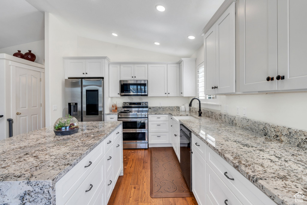 Kitchen with appliances with stainless steel finishes, vaulted ceiling, white cabinetry, light stone counters, and recessed lighting