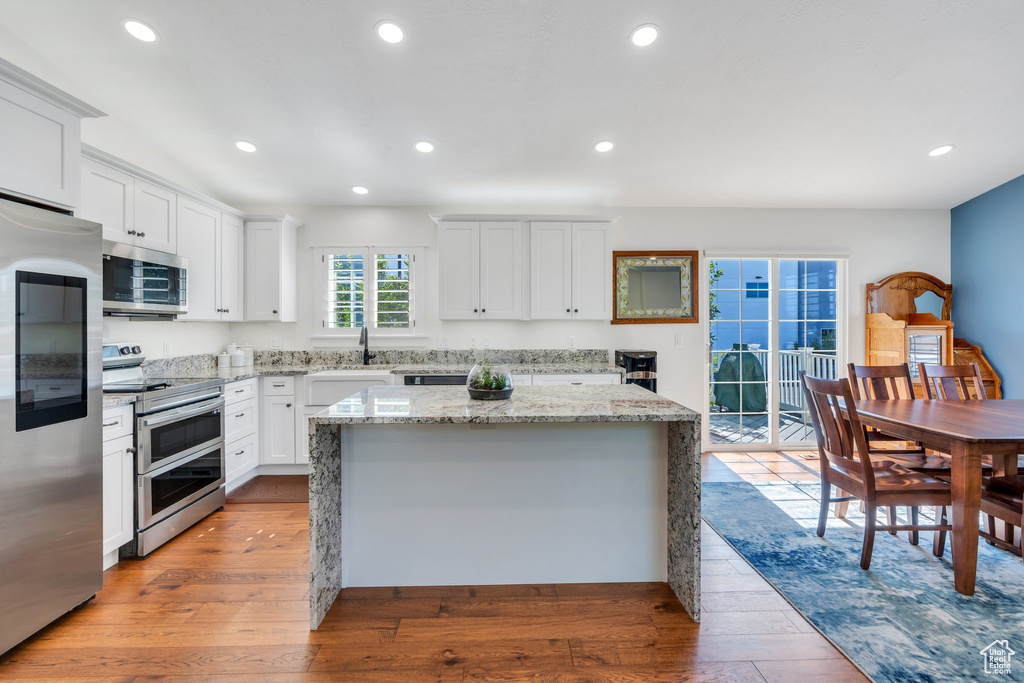 Kitchen with appliances with stainless steel finishes, light wood finished floors, a center island, white cabinets, and recessed lighting