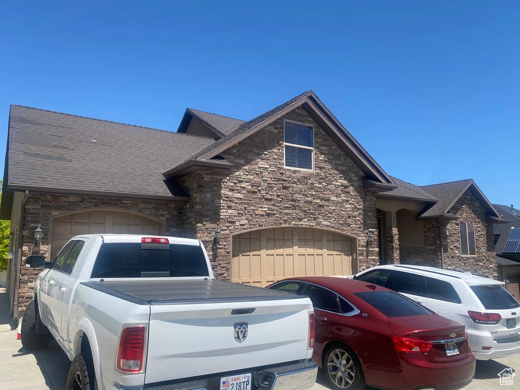 View of front of property with stone siding, a garage, driveway, and a shingled roof