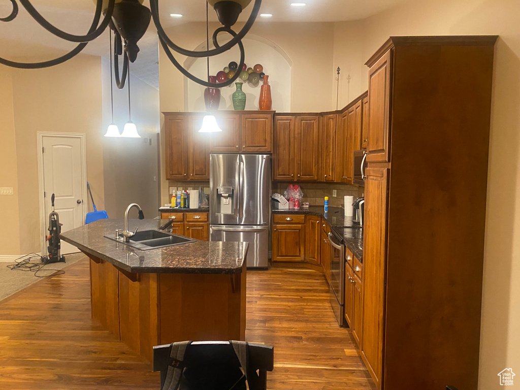 Kitchen featuring appliances with stainless steel finishes, an island with sink, dark wood-type flooring, tasteful backsplash, and a breakfast bar area