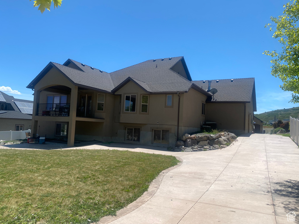 Rear view of house featuring a balcony, stucco siding, a patio, and roof with shingles
