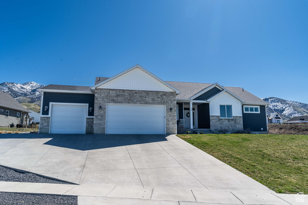View of front of property featuring stone siding, a mountain view, a garage, and a front yard
