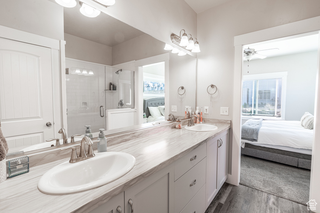 Bathroom with connected bathroom, double vanity, wood finished floors, ceiling fan, and a stall shower