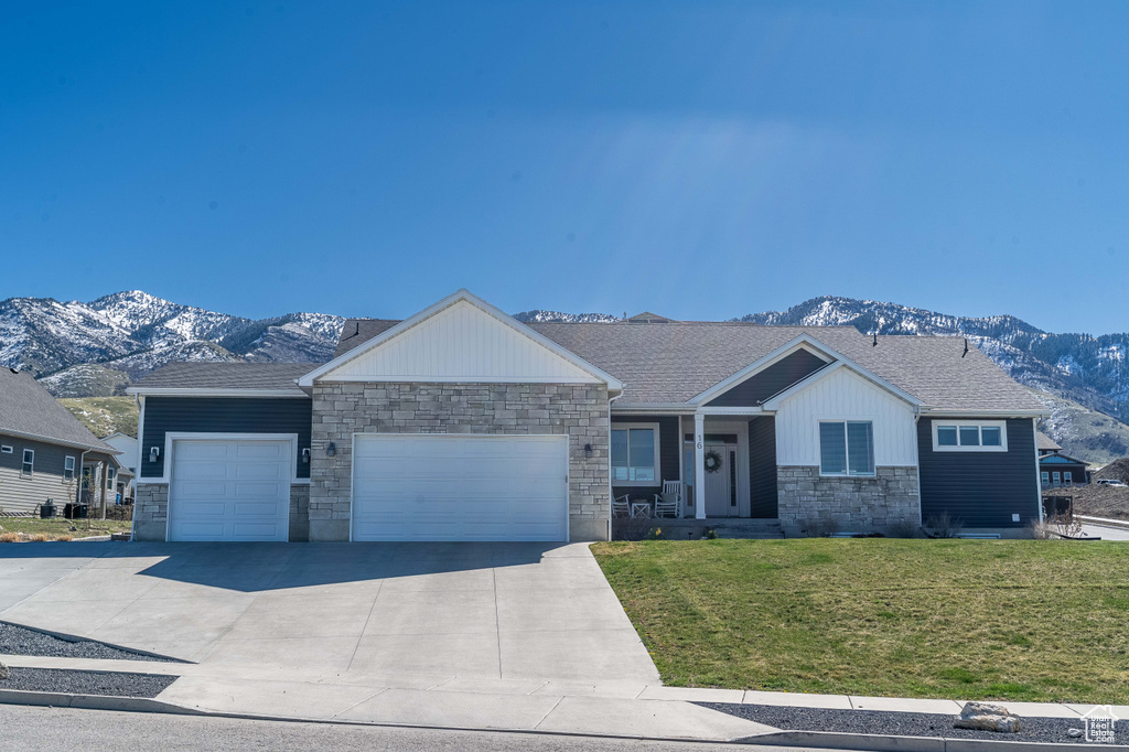Single story home featuring a mountain view, an attached garage, stone siding, a front yard, and concrete driveway