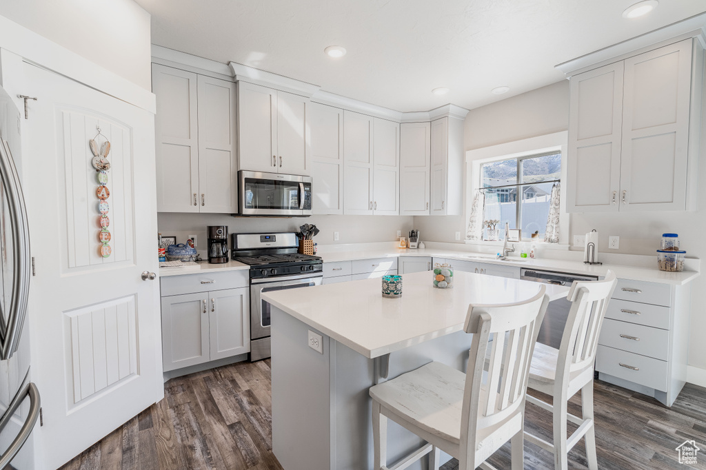 Kitchen featuring appliances with stainless steel finishes, a breakfast bar area, dark wood finished floors, a center island, and light countertops