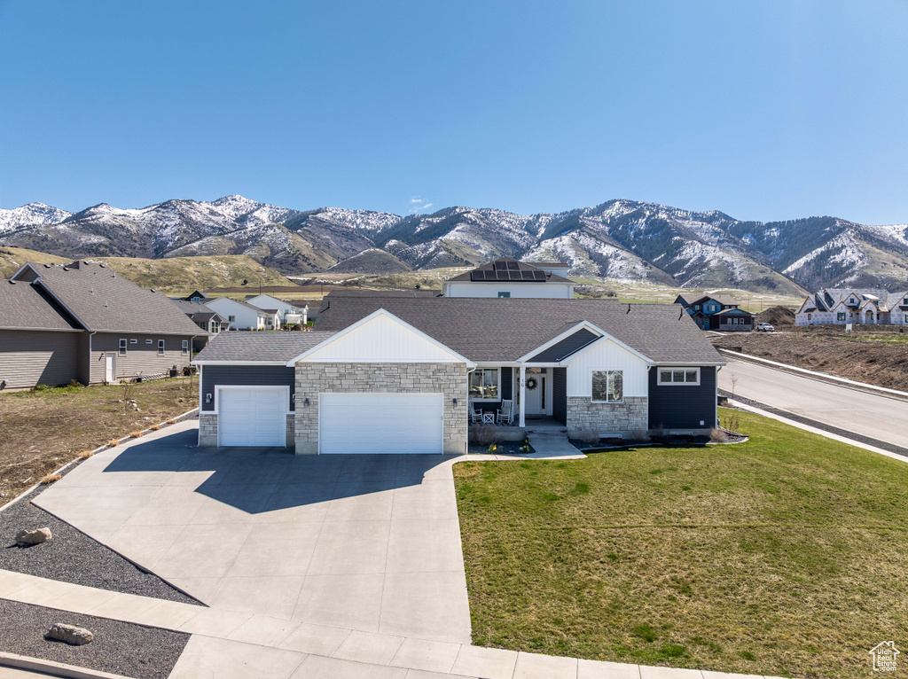 Ranch-style home with a mountain view, stone siding, a garage, driveway, and a front yard