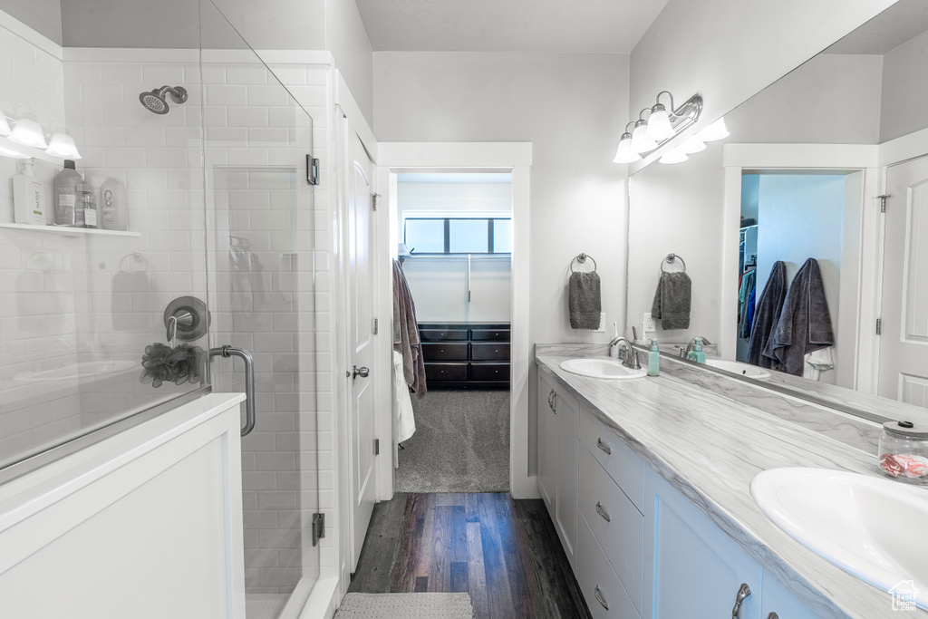 Bathroom featuring double vanity, wood finished floors, a shower stall, and a spacious closet