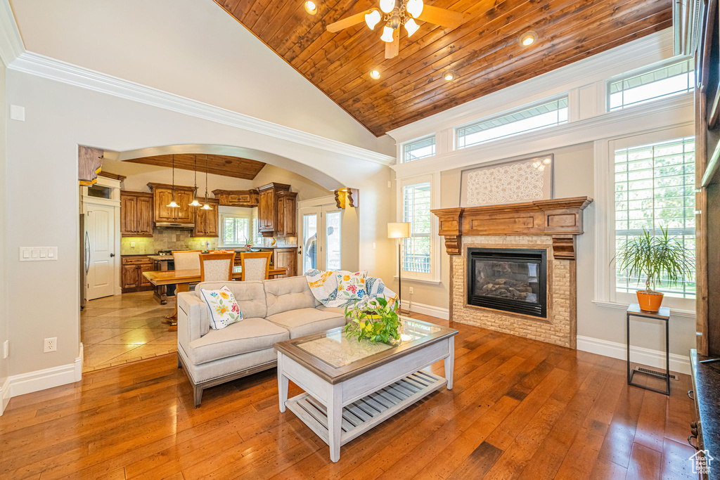 Living room featuring ceiling fan, a glass covered fireplace, arched walkways, hardwood / wood-style floors, and wood ceiling