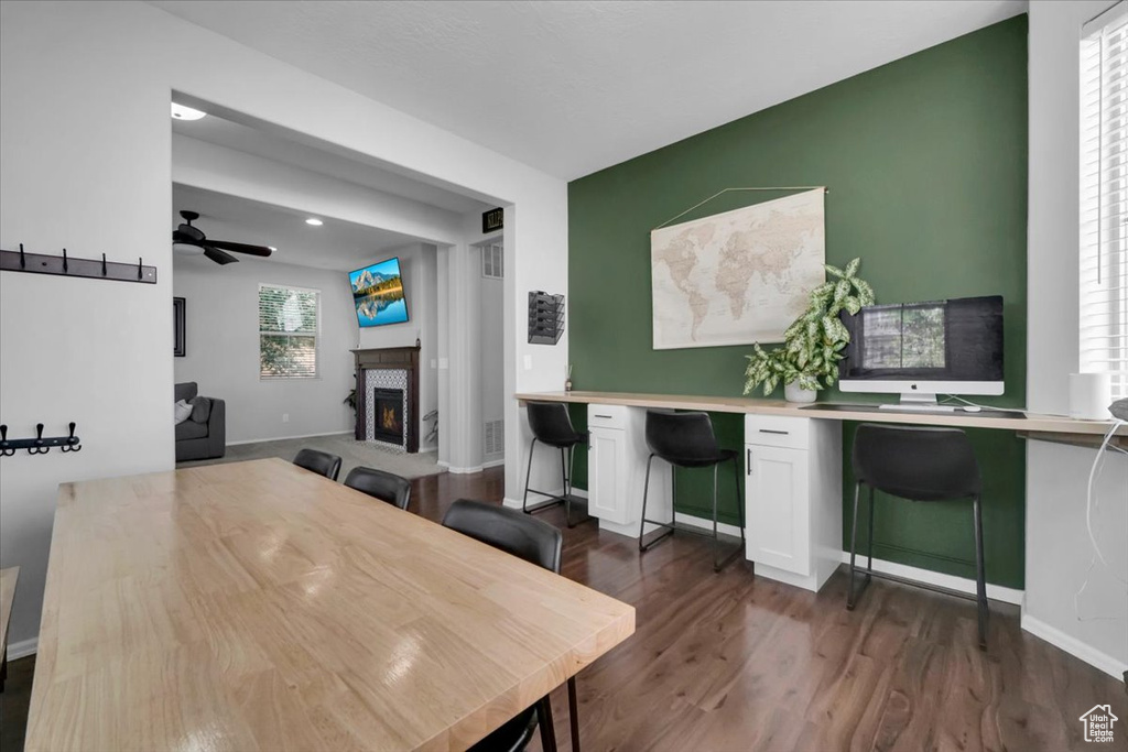 Dining room featuring a lit fireplace, dark wood finished floors, a ceiling fan, a desk, and recessed lighting