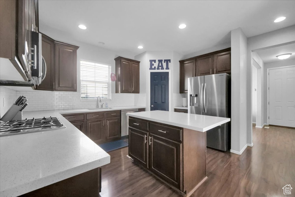 Kitchen with appliances with stainless steel finishes, backsplash, dark wood-style flooring, a kitchen island, and dark brown cabinets