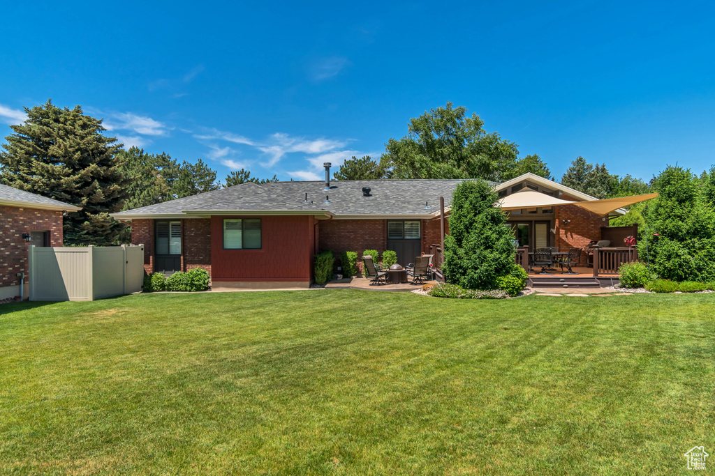 Back of house featuring a deck, brick siding, a patio, and roof with shingles