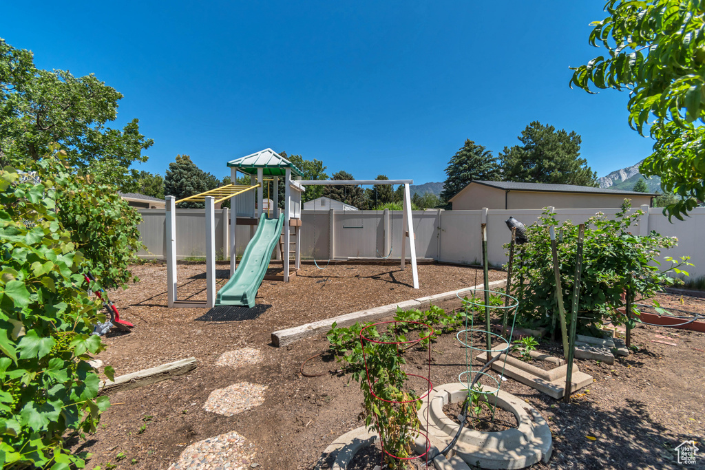 View of playground featuring a fenced backyard and a vegetable garden