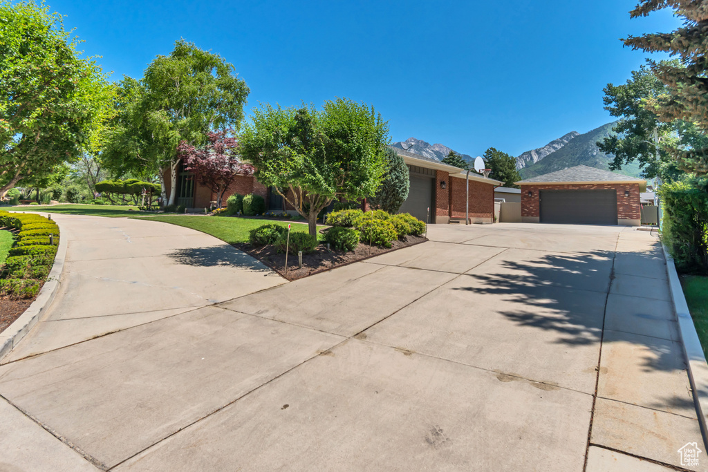 View of property hidden behind natural elements featuring driveway, brick siding, a mountain view, and a garage