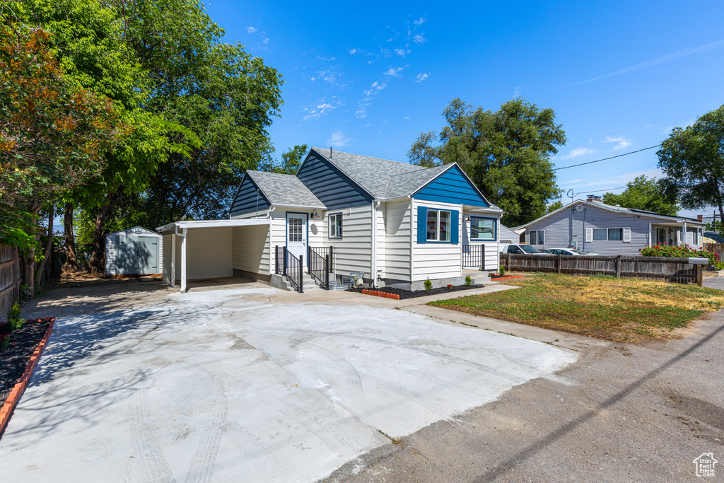 View of front of home featuring concrete driveway, a carport, a storage shed, a shingled roof, and entry steps