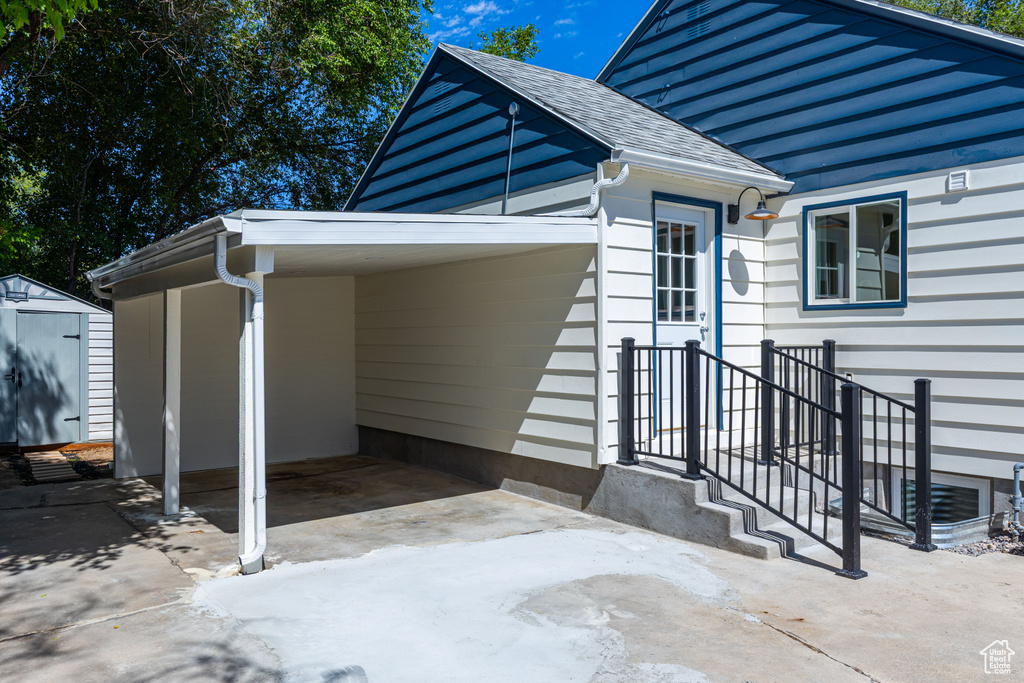 View of side of property with a storage shed, concrete driveway, roof with shingles, and a carport
