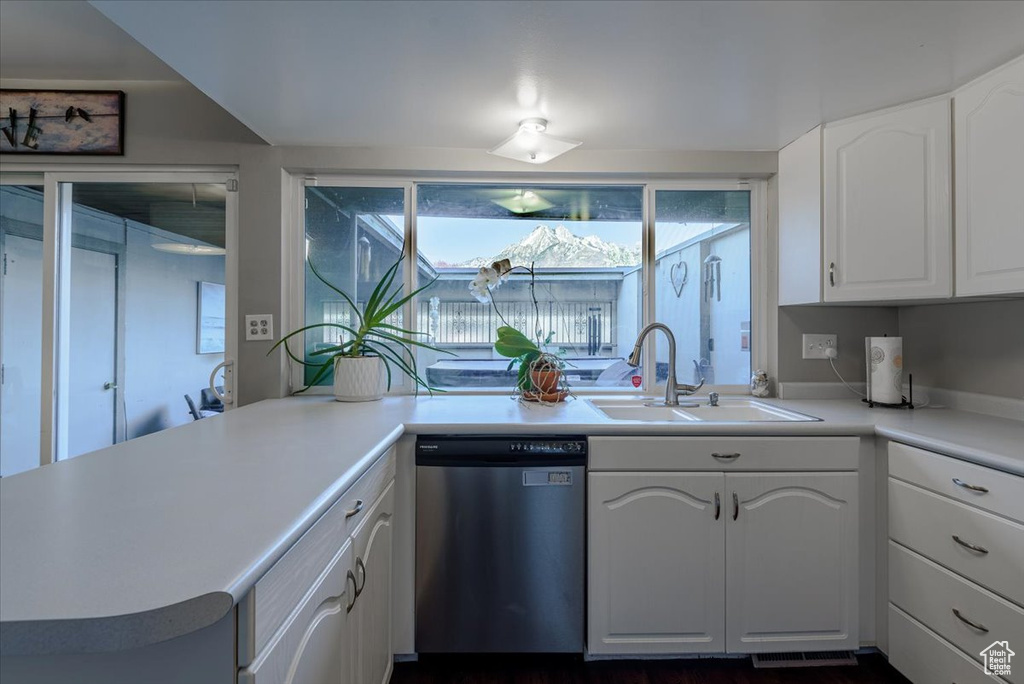 Kitchen featuring stainless steel dishwasher, a sink, white cabinets, and light countertops