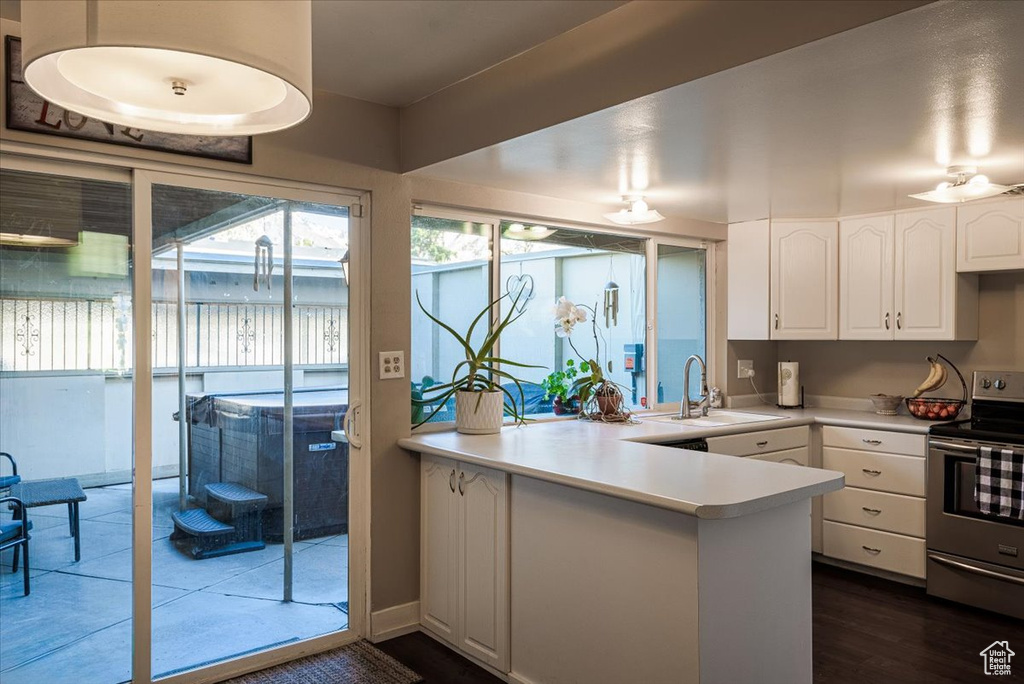 Kitchen featuring stainless steel electric range, a sink, white cabinetry, a peninsula, and light countertops