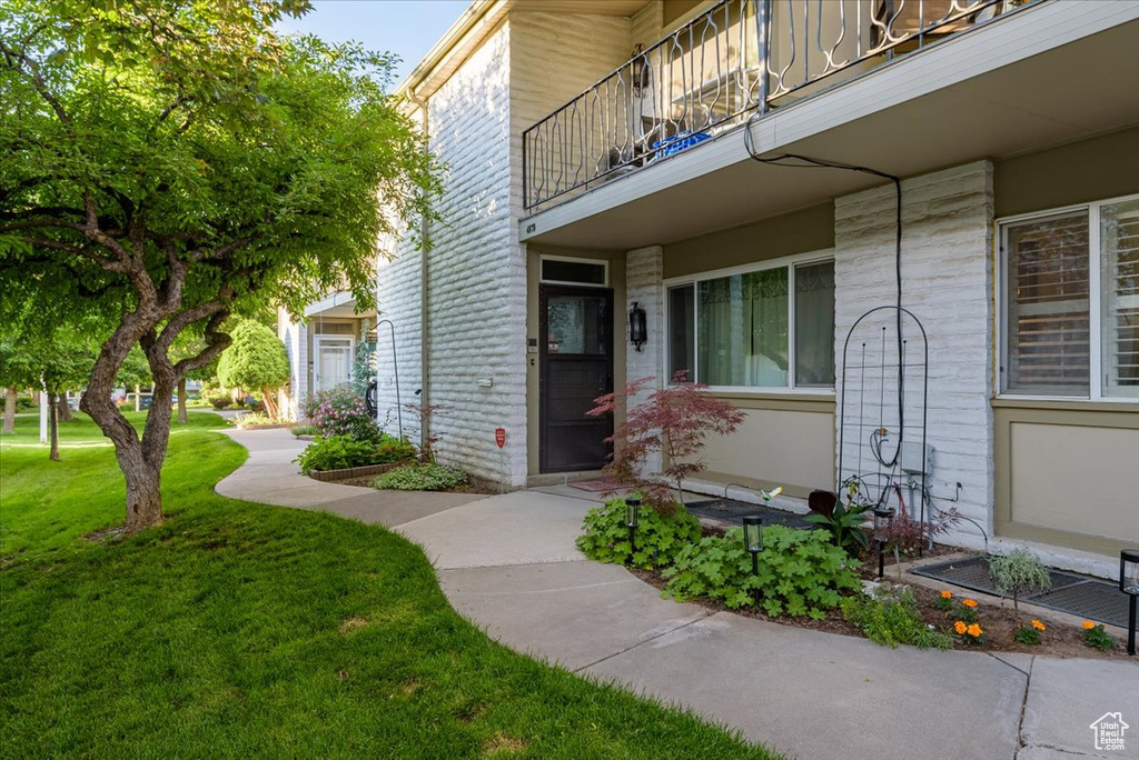 View of exterior entry with a balcony and a yard