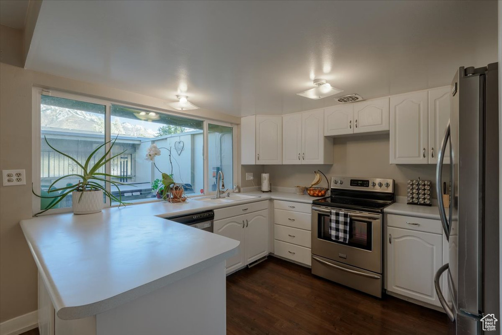 Kitchen with appliances with stainless steel finishes, a sink, a peninsula, and white cabinets