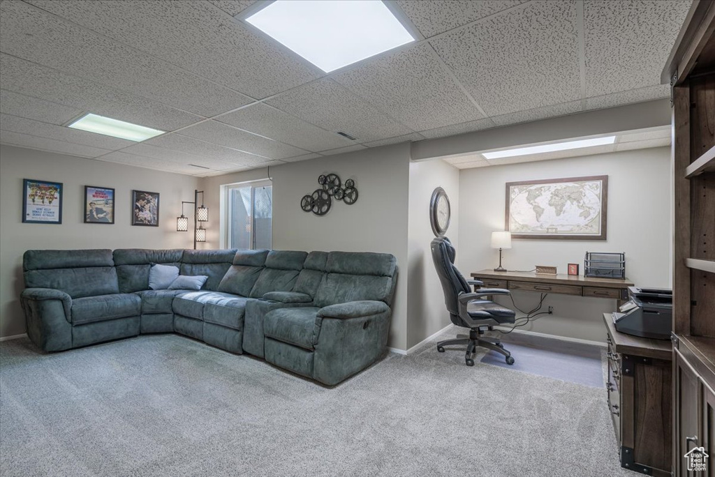 Carpeted living room featuring a desk, a drop ceiling, and baseboards