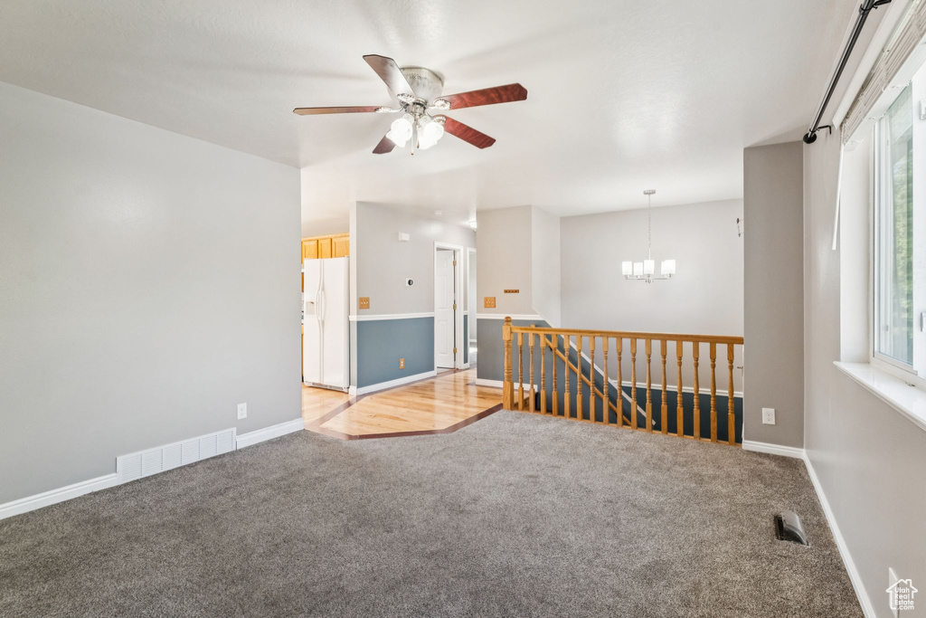 Empty room with light colored carpet, a chandelier, and a ceiling fan