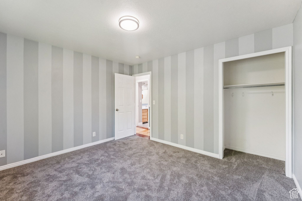 Unfurnished bedroom with carpet, wallpapered walls, and a closet