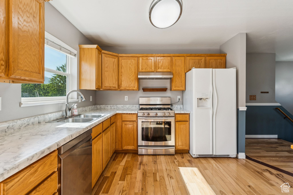 Kitchen with appliances with stainless steel finishes, exhaust hood, light wood-style floors, and light stone countertops