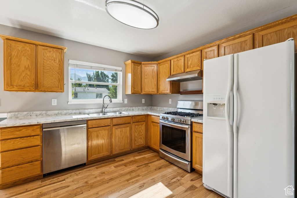 Kitchen with stainless steel appliances, under cabinet range hood, light wood-type flooring, light stone countertops, and brown cabinetry