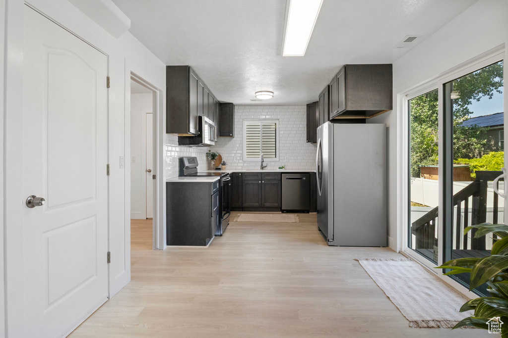 Kitchen featuring stainless steel appliances, light wood finished floors, decorative backsplash, and light countertops