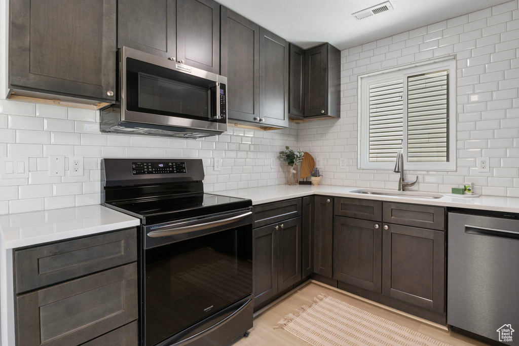 Kitchen with stainless steel appliances, light countertops, decorative backsplash, and dark brown cabinetry