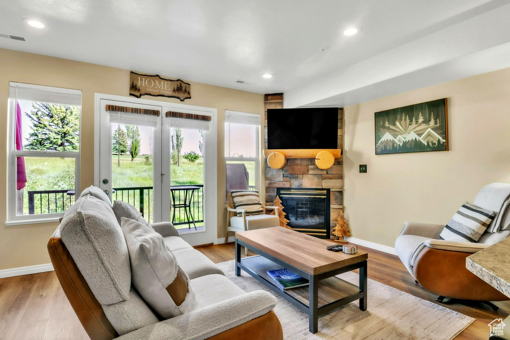 Living area featuring a stone fireplace, healthy amount of natural light, french doors, wood finished floors, and recessed lighting