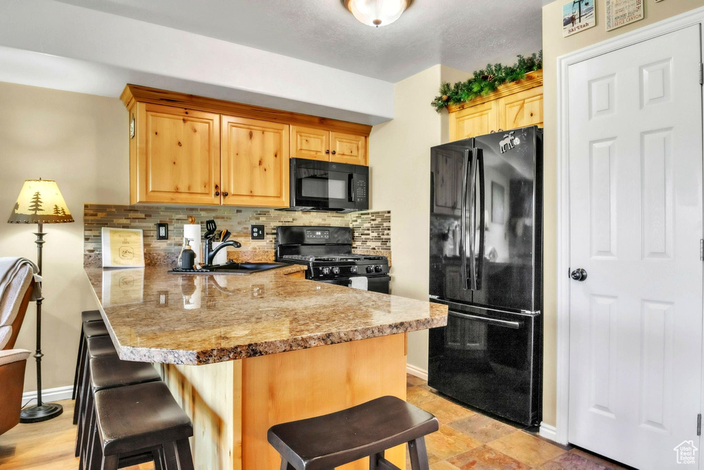 Kitchen with black appliances, a kitchen breakfast bar, a peninsula, backsplash, and light brown cabinetry