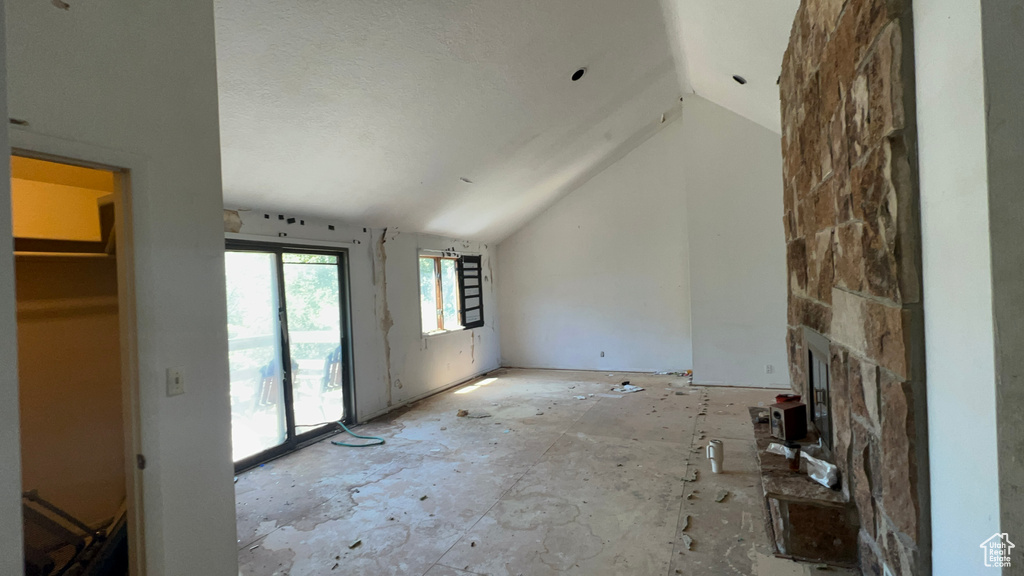 Unfurnished living room with vaulted ceiling and a stone fireplace