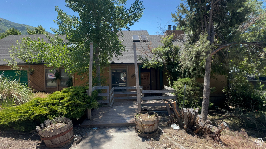 View of property hidden behind natural elements featuring a shingled roof and a chimney