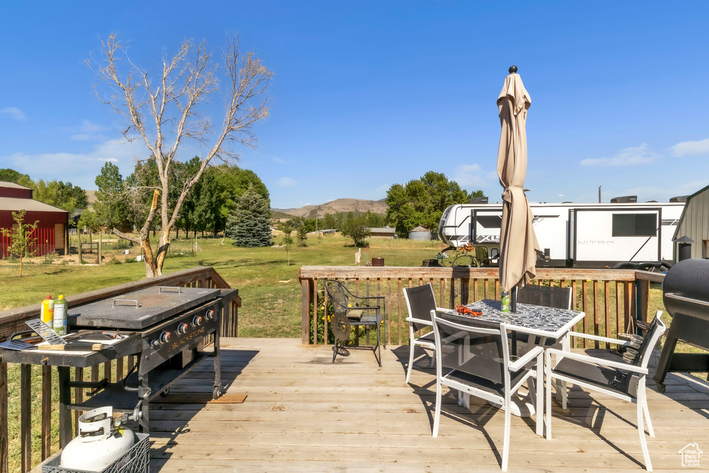 Wooden terrace with outdoor dining space, a lawn, and a mountain view