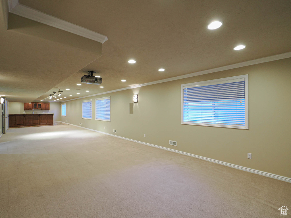 Basement with crown molding, recessed lighting, light colored carpet, healthy amount of natural light, and bar