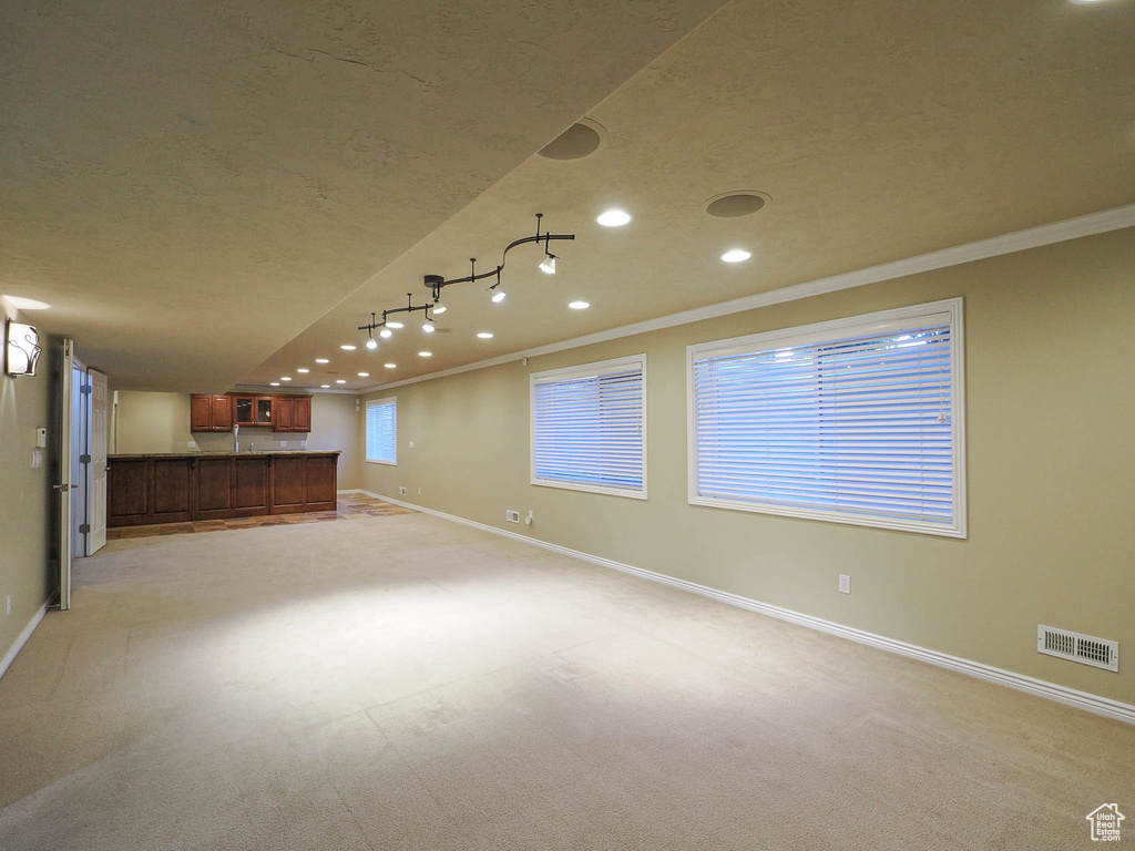 Basement with ornamental molding, a textured ceiling, recessed lighting, light colored carpet, and bar area