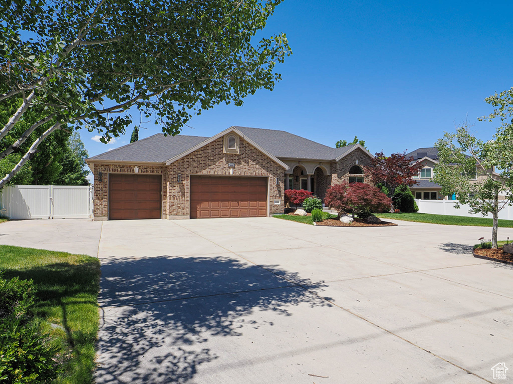 View of front of property with a garage, driveway, brick siding, a shingled roof, and a gate