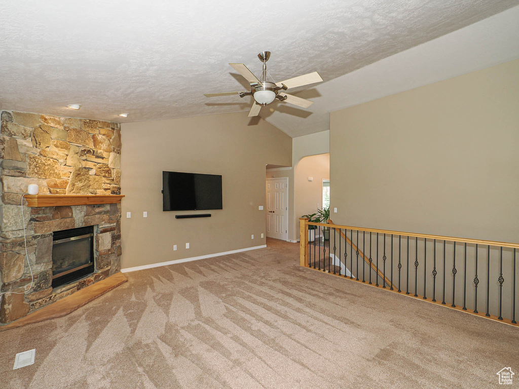 Unfurnished living room featuring lofted ceiling, ceiling fan, carpet, a textured ceiling, and a stone fireplace