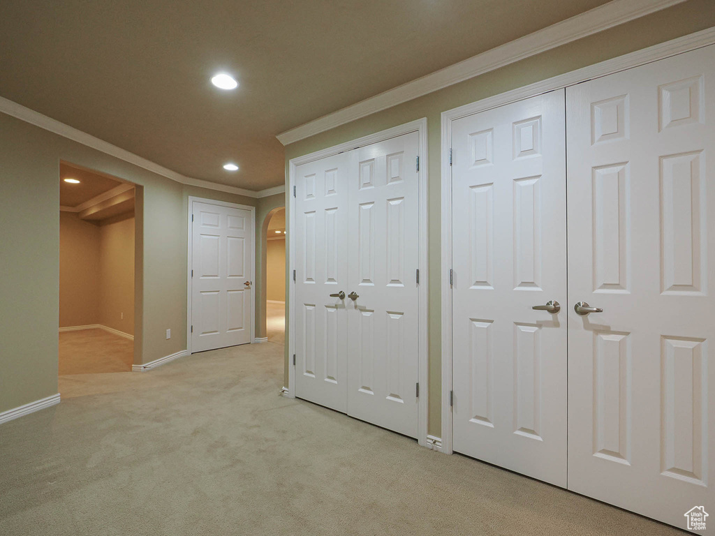 Unfurnished bedroom featuring two closets, crown molding, recessed lighting, light colored carpet, and arched walkways